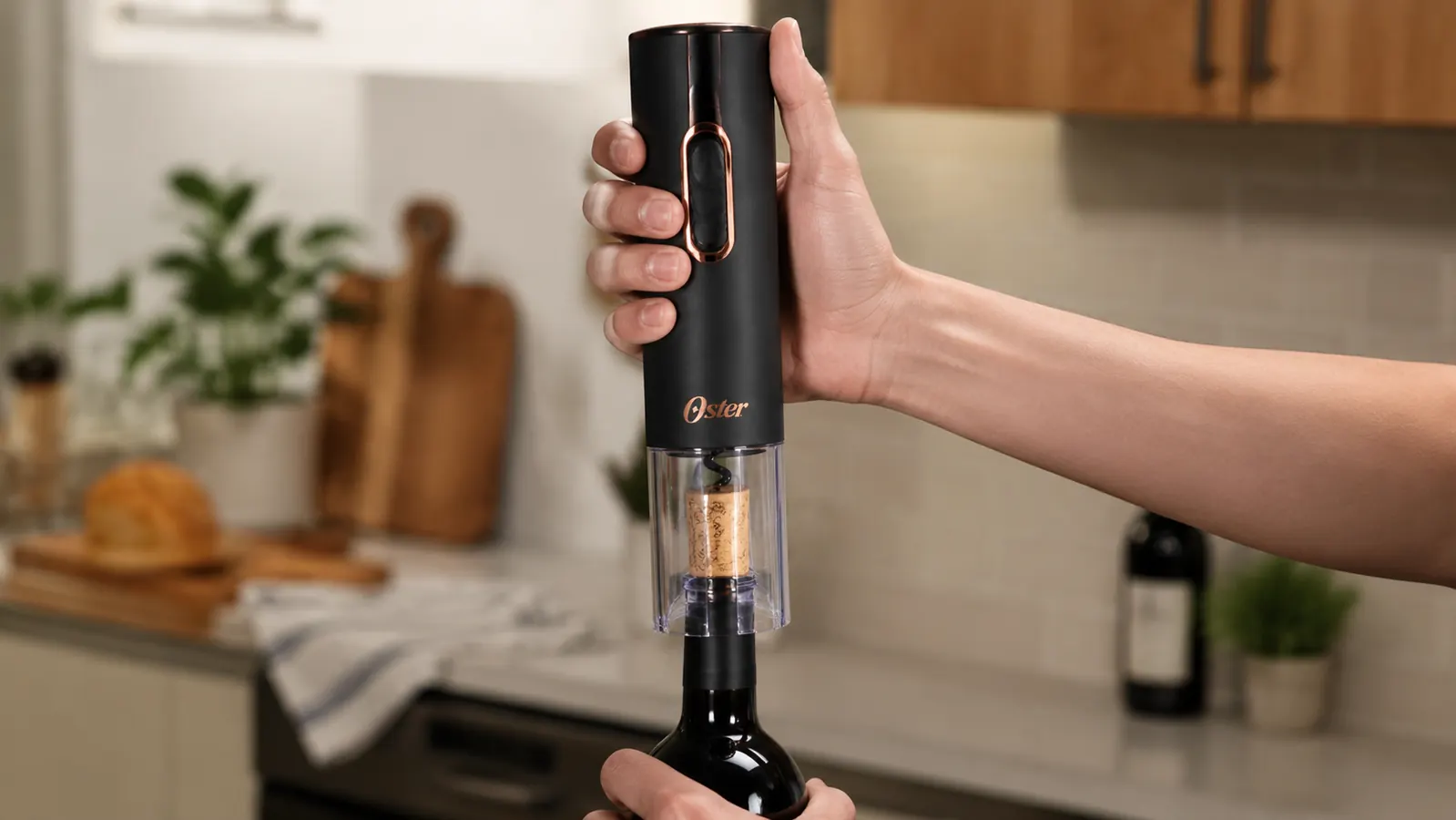 Hand holding the Oster electric wine opener straight down onto the top of an open bottle while the motor pulls the cork